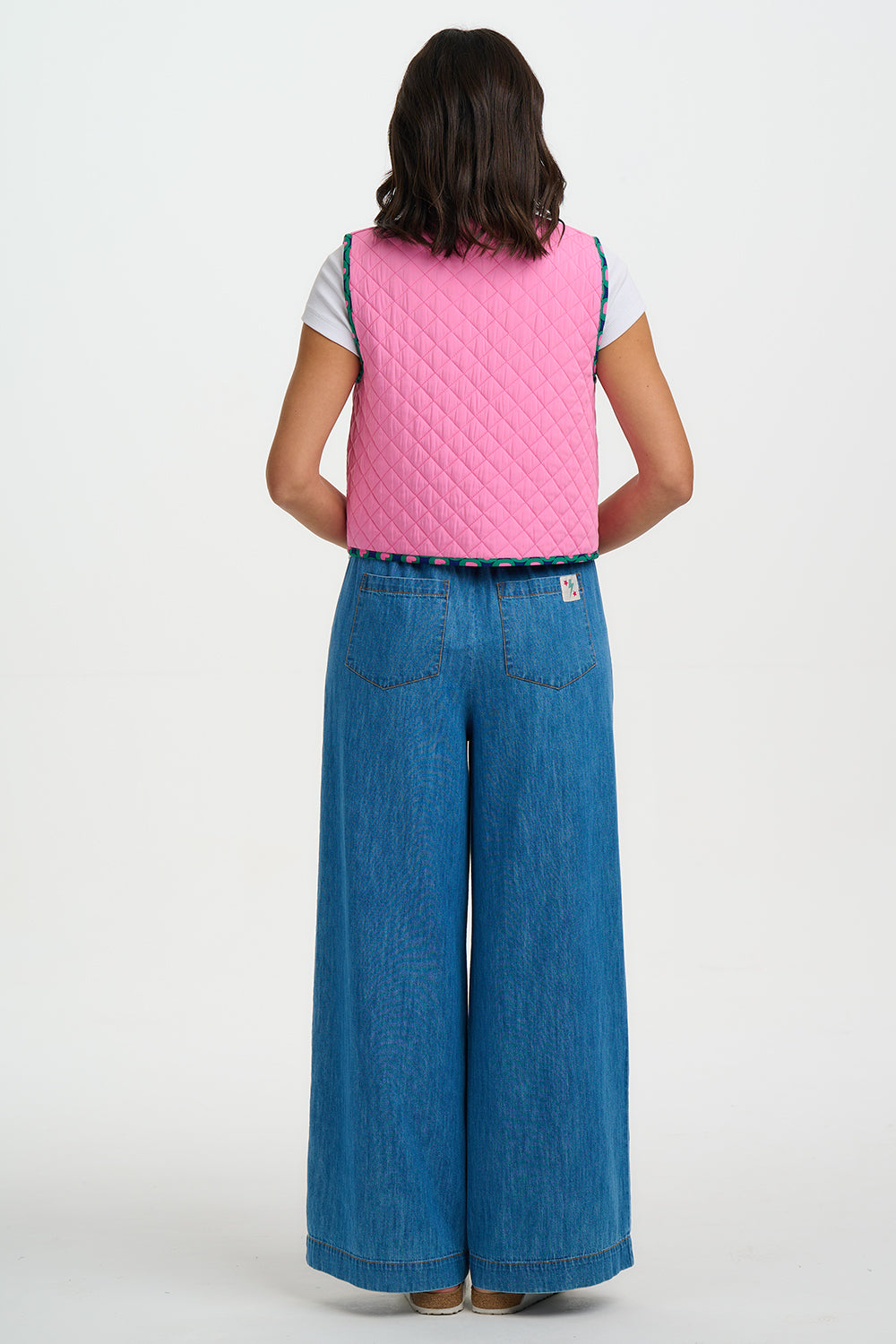 Person wearing a pink quilted vest and blue jeans on a white background