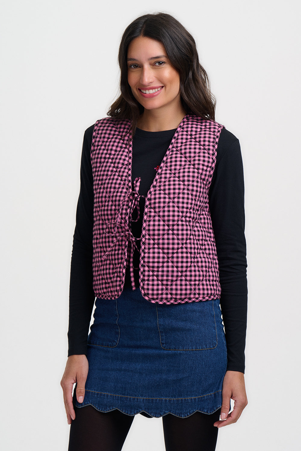 Woman wearing a checkered vest over a black top and blue skirt on a white background