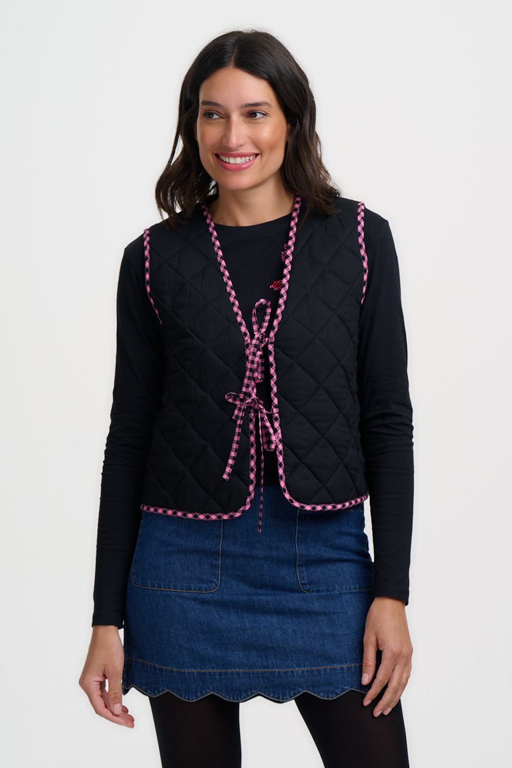 Woman wearing a black quilted vest with pink trim on a white background