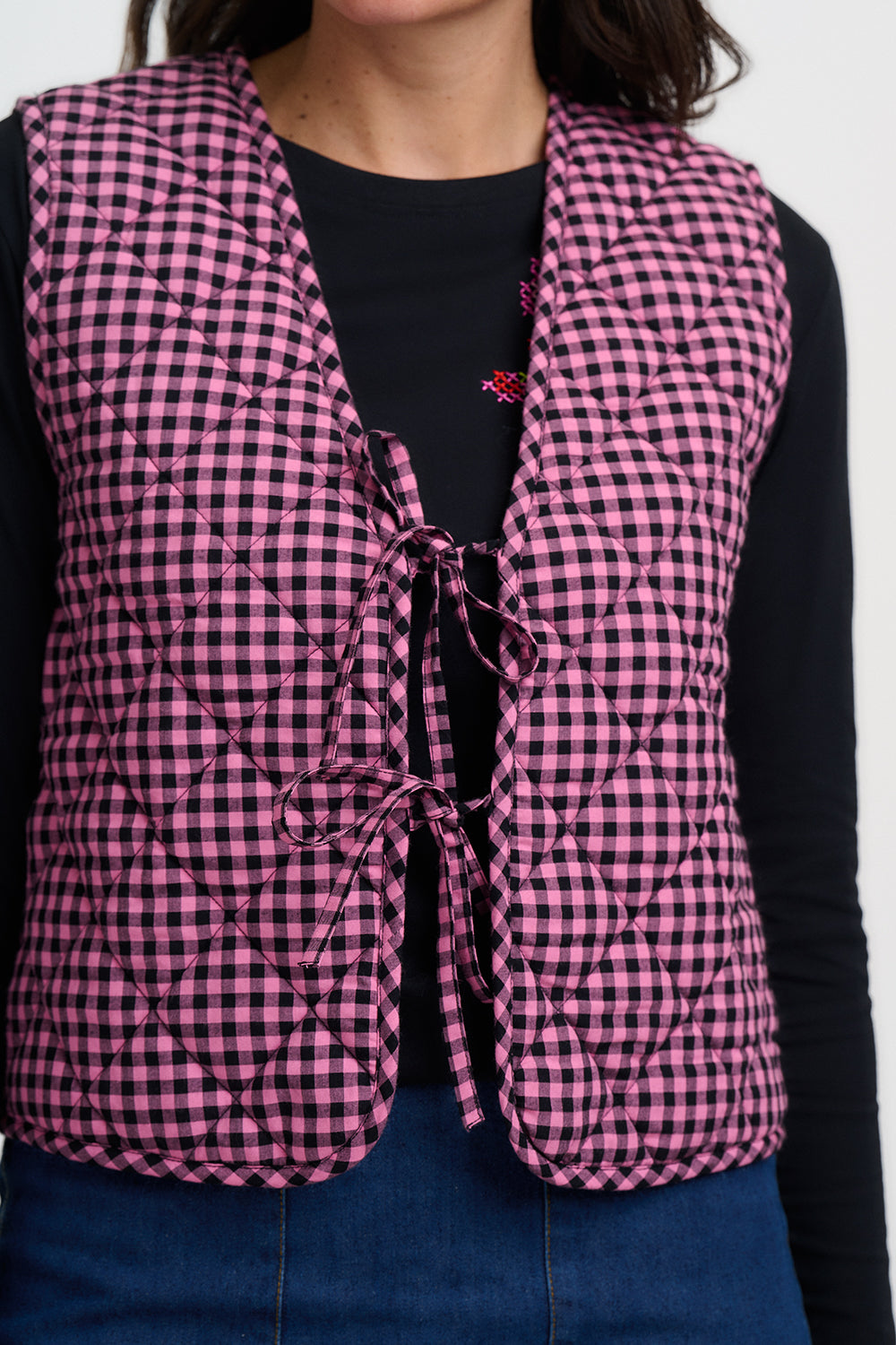 Person wearing a pink and black checkered vest over a black shirt on a white background