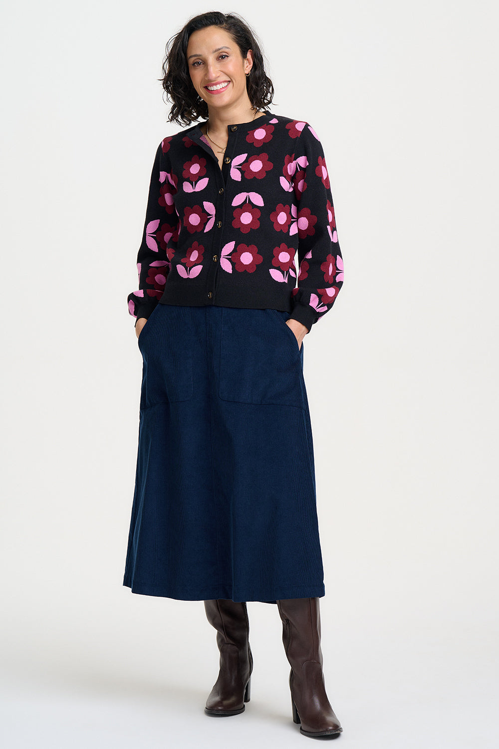 Woman wearing a black floral blouse and navy skirt with brown boots on a white background