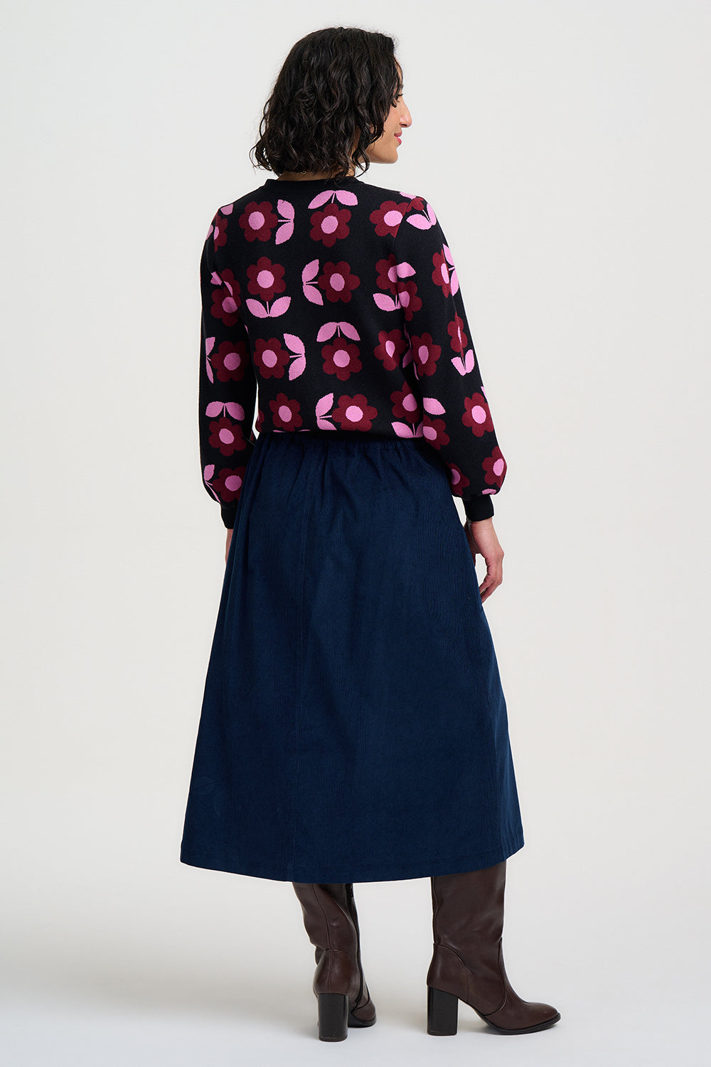 Person wearing a patterned sweater and navy skirt on a white background