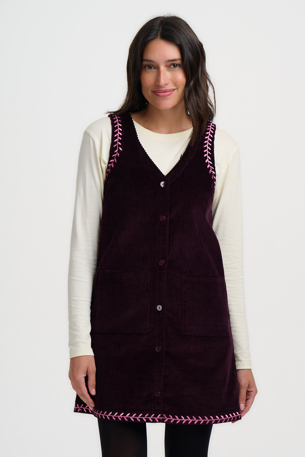 Woman wearing a dark purple corduroy apron with decorative trim on a white background