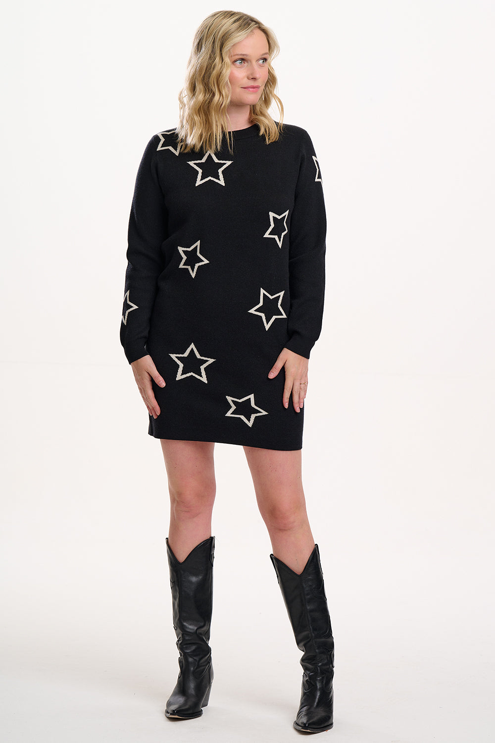 Woman wearing a black dress with star patterns and black boots on a white background