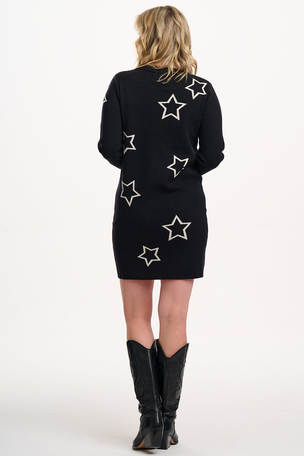 Woman wearing a black dress with star patterns and black boots on a white background