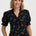 Woman wearing a black floral blouse with colorful flowers on a white background