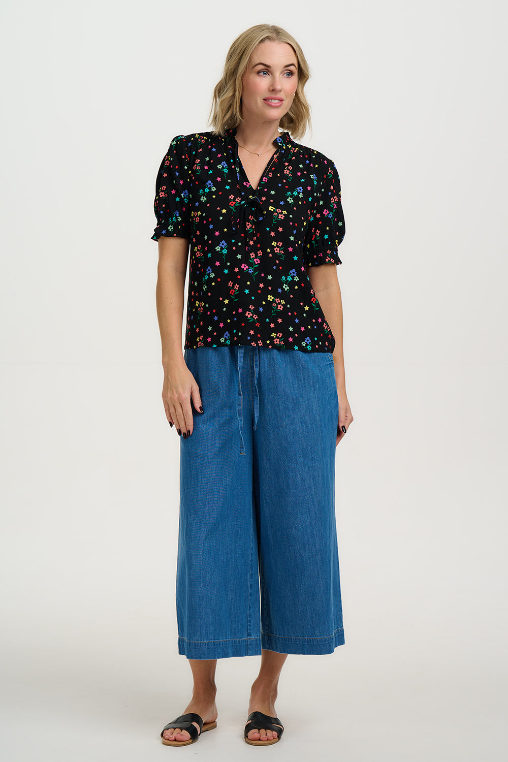 Woman wearing a black floral blouse and blue jeans on a white background