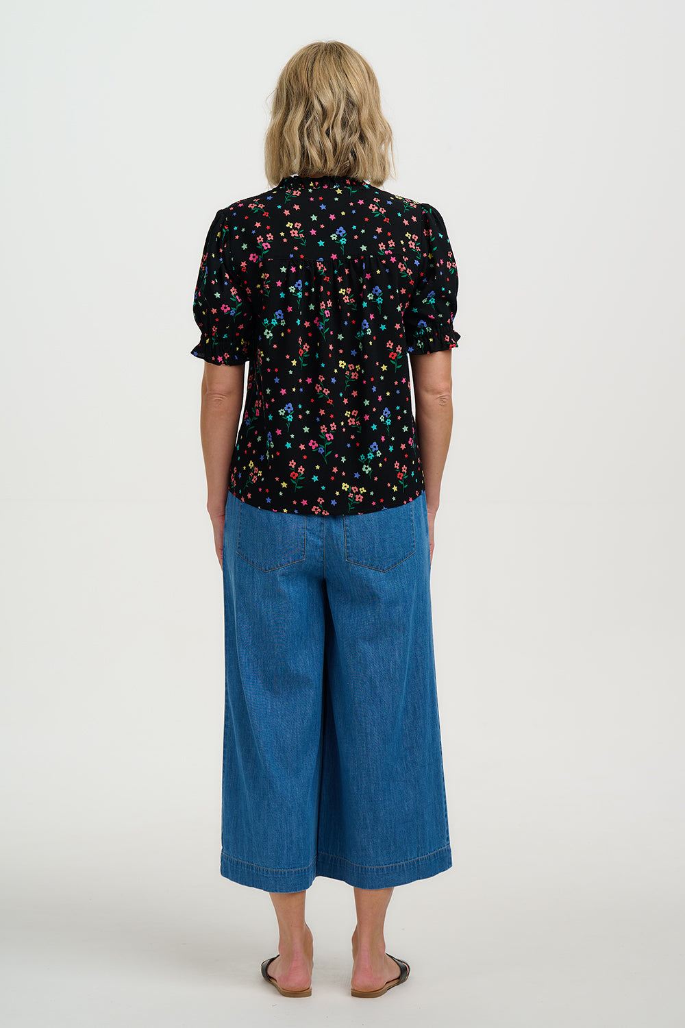 Person wearing a black floral shirt and blue jeans on a white background