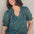 A woman smiling and wearing a green blouse with a geometric concentric circles pattern, featuring a frill collar and v-neckline with ties, short puff sleeves with elasticated frill cuffs.