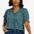 A woman modeling a green shirt with a geometric concentric circles pattern, featuring a frill collar and ties at the neckline, short puff sleeves with elasticated frill cuffs, and a v-neckline.