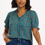 A woman modeling a green shirt with a geometric concentric circles pattern, featuring a frill collar and ties at the neckline, short puff sleeves with elasticated frill cuffs, and a v-neckline.