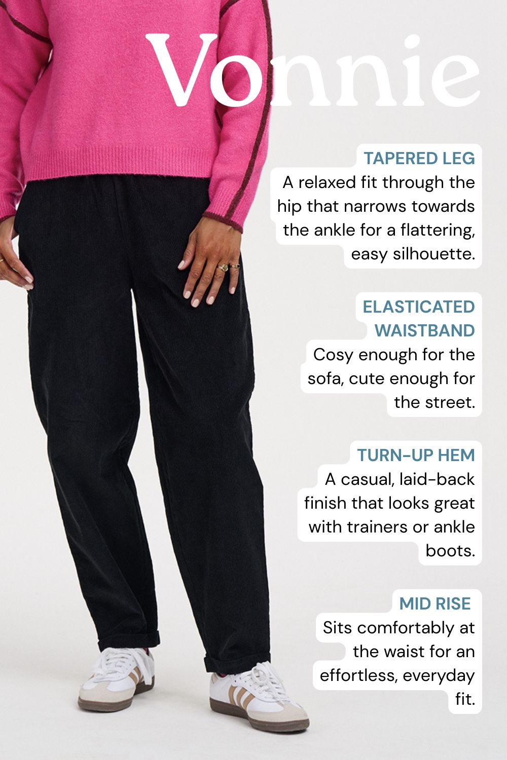 A person wearing black tapered mid-rise pants with a pink sweater and white sneakers, shown against a light gray studio background with descriptive text callouts about the fit and waistband.