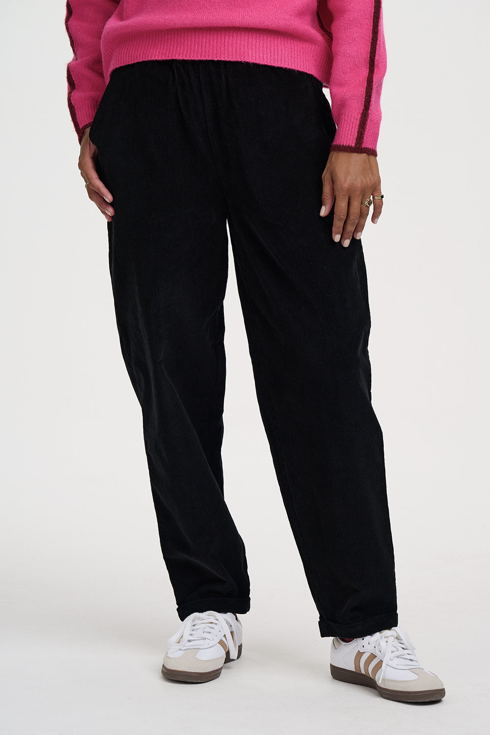 A person wearing loose black pants with a pink ribbed sweater and white sneakers, shown from the chest down against a plain light background.