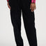 A person wearing loose black pants with a pink ribbed sweater and white sneakers, shown from the chest down against a plain light background.
