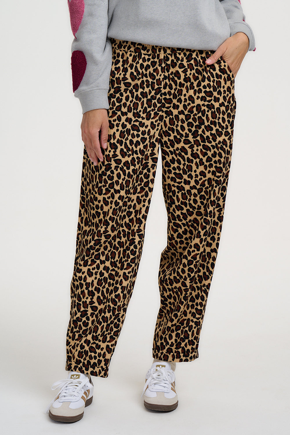 Person wearing leopard print pants and white sneakers on a white background