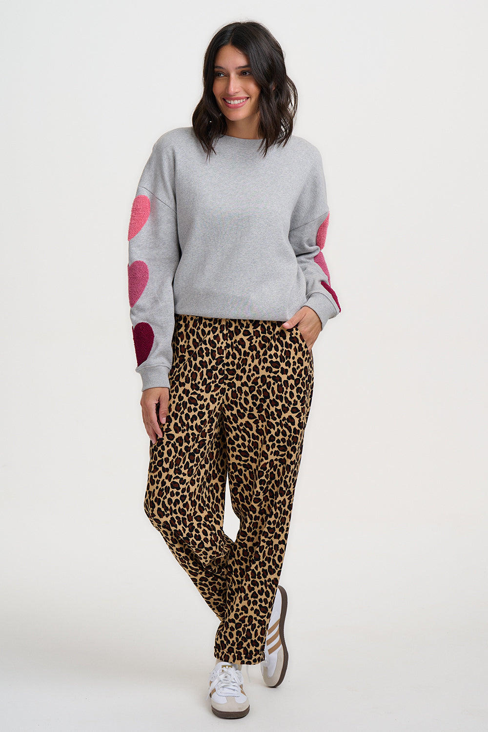 Woman wearing a gray sweater with pink sleeves and leopard print pants on a white background