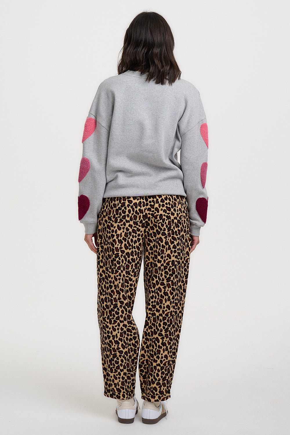 Person wearing a gray sweater with red heart patterns and leopard print pants on a white background