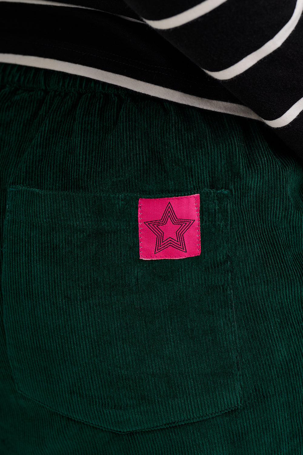 Green corduroy trousers with a pink label featuring a star design.