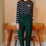 Woman wearing a striped shirt and green pants standing in a room with wooden furniture.
