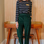 Woman wearing a striped shirt and green pants standing in a room with wooden furniture.