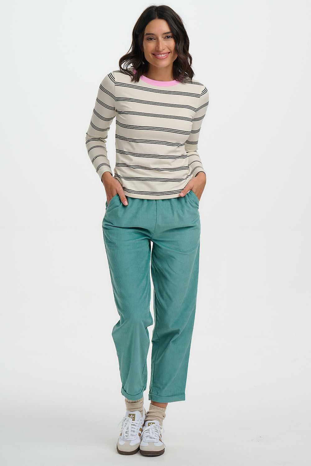Woman wearing a striped sweater and teal pants on a white background