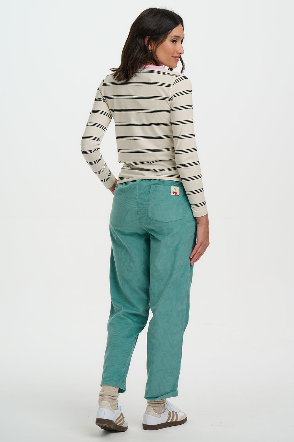 Woman wearing a striped shirt and teal pants on a white background