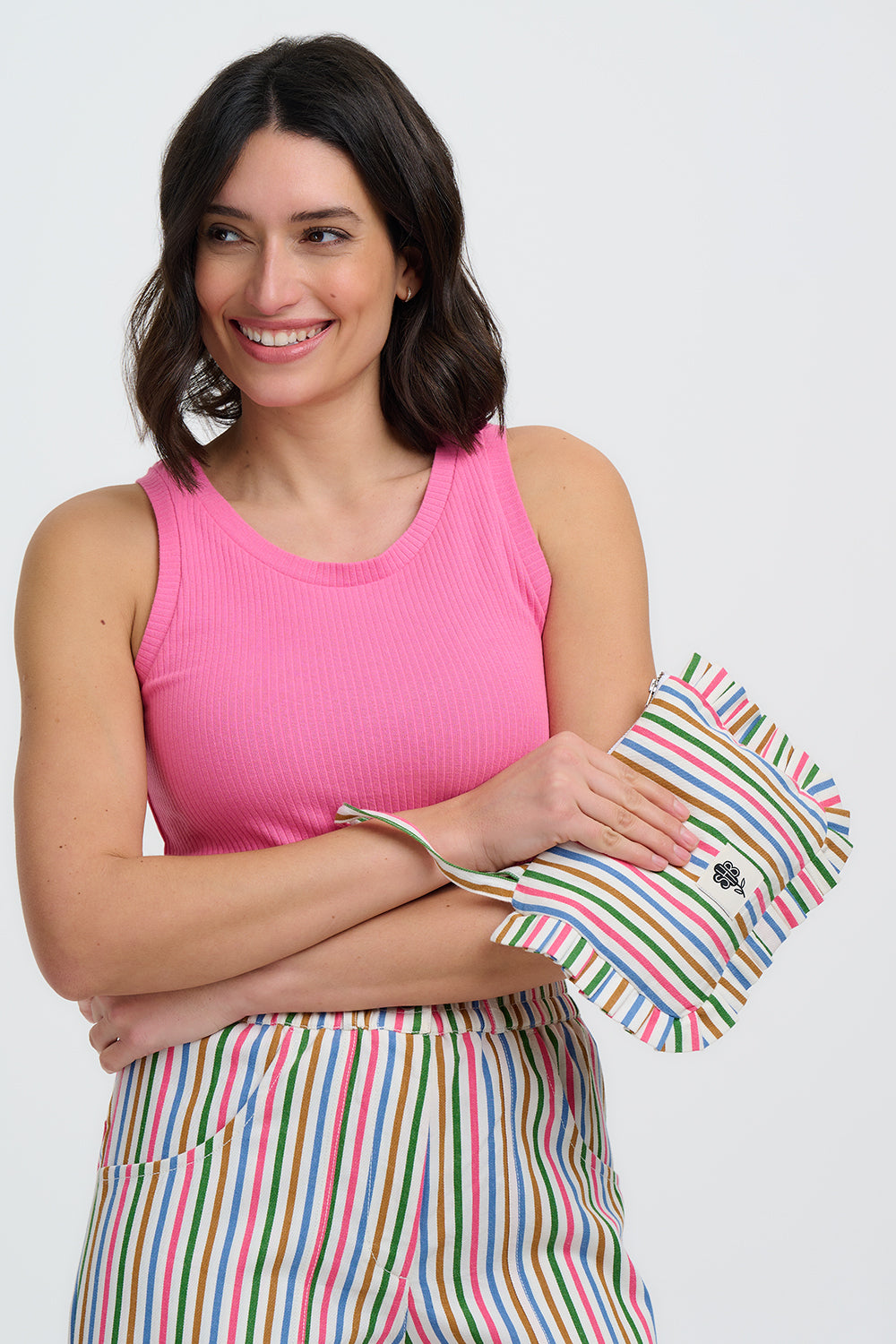 Woman wearing a pink sleeveless top and colorful striped skirt holding a striped clutch.