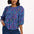 A model wearing a blue blouse with horizontal multicolor lines and 3/4 blouson sleeves.