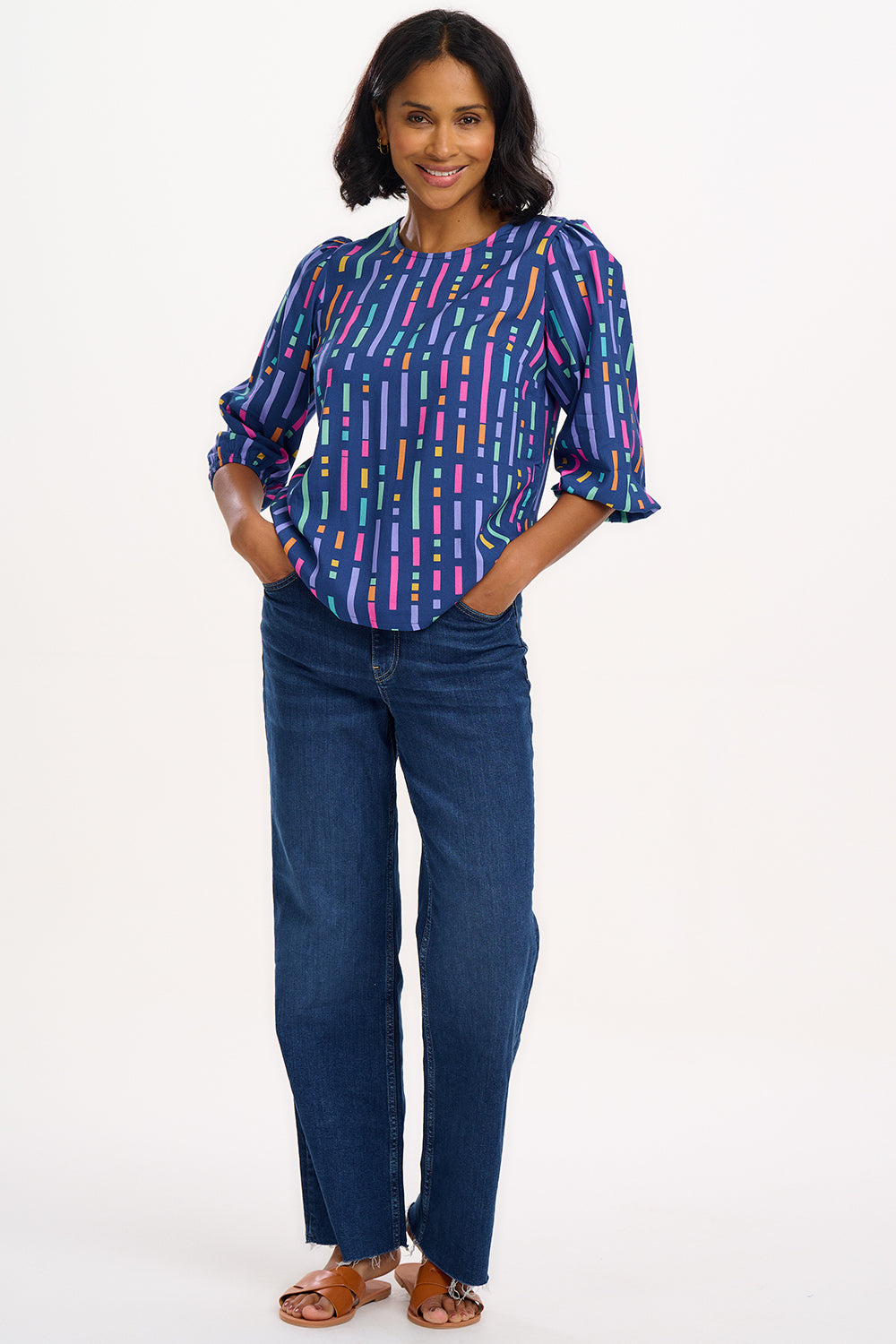 A model wearing a blue blouse with horizontal multicolor lines and 3/4 blouson sleeves.