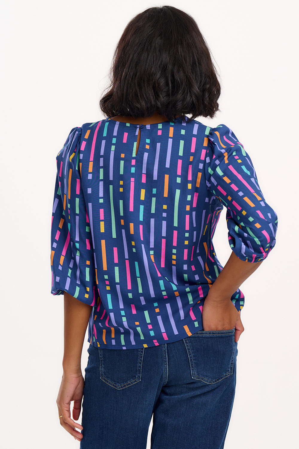 A model wearing a blue blouse with horizontal multicolor lines and 3/4 blouson sleeves.