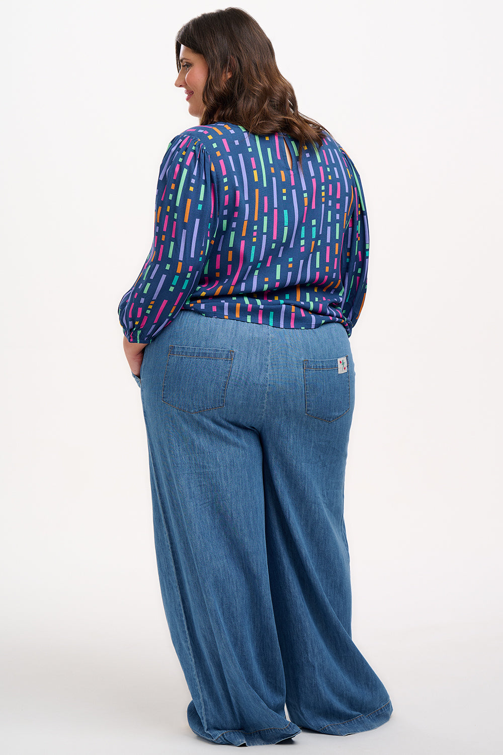 A model wearing a blue blouse with horizontal multicolor lines and 3/4 blouson sleeves.