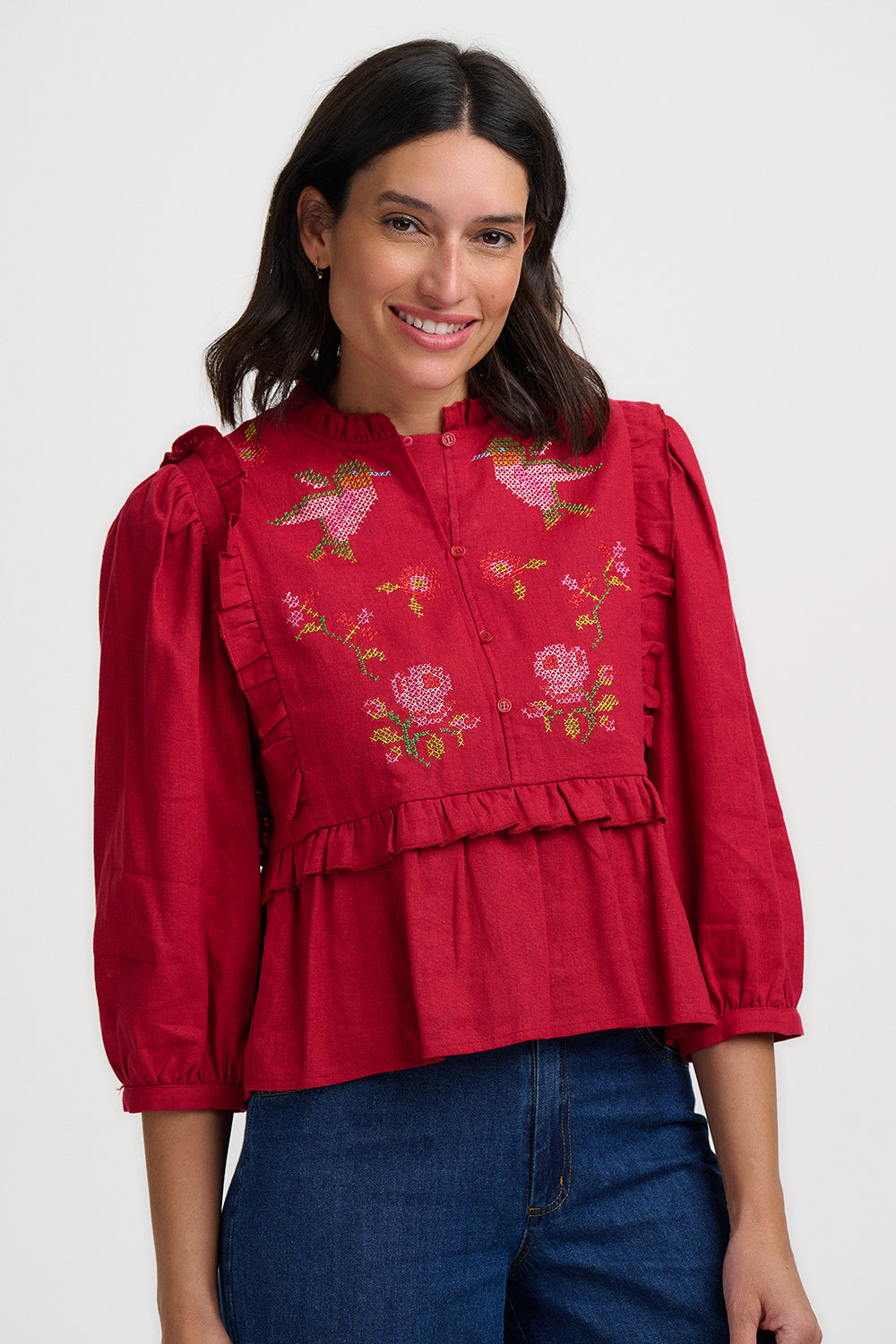 Woman wearing a red embroidered blouse with blue jeans on a white background