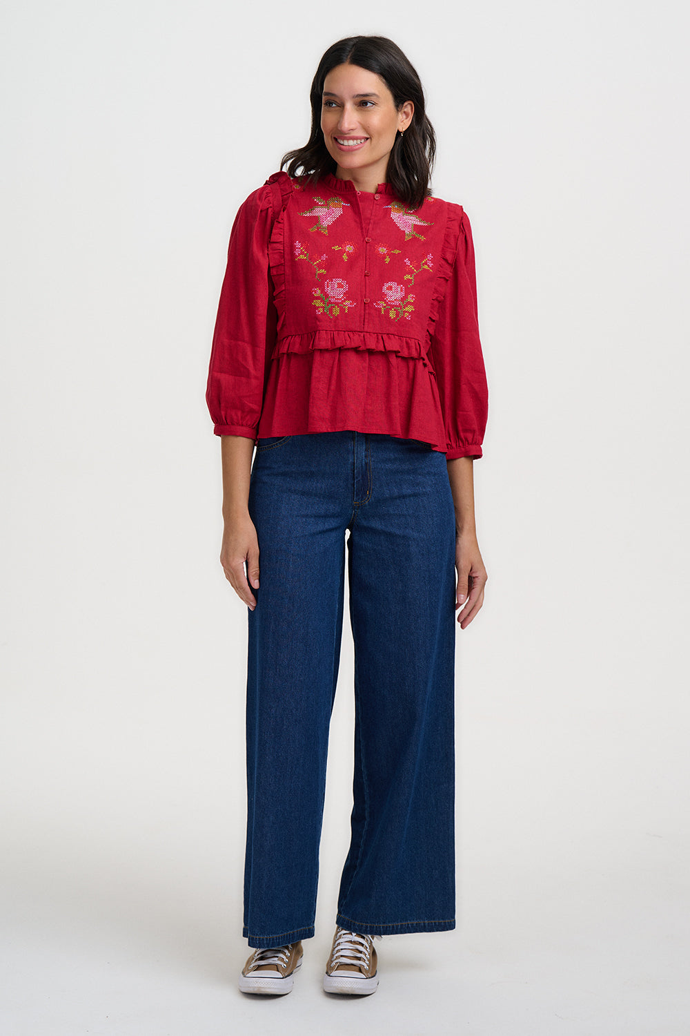Woman wearing a red embroidered blouse and blue jeans on a white background