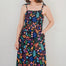 A model wearing a midi length jersey dress with a shirred bodice and tie shoulder straps. The dress has a black base with a colorful jungle spirit design featuring wildlife and foliage.