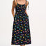 A woman wearing a midi-length black sundress with a colorful pattern, featuring tie shoulder straps and a shirred bodice, standing against a white background.