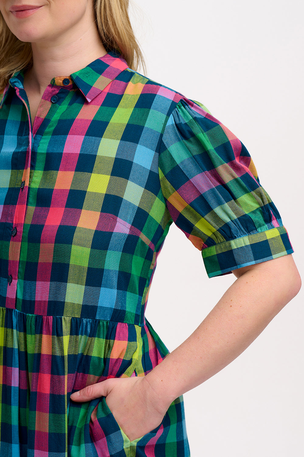 A woman wearing a midi smock dress with a checkered pattern in shades of pink, green, and blue.