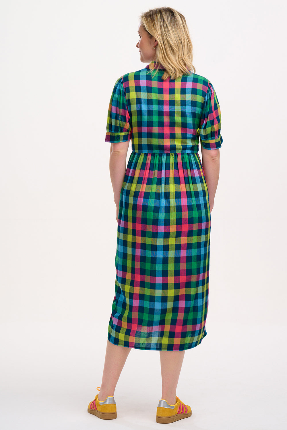 A woman standing and wearing a midi smock dress with a classic shirt bodice and short puff sleeves, featuring a geometric pattern in shades of pink, green, and blue.