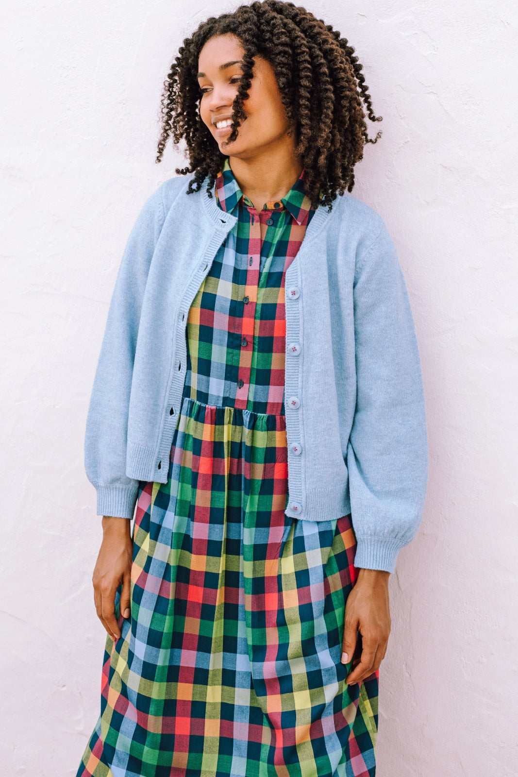 Woman wearing a colorful plaid dress with a light blue cardigan against a white background