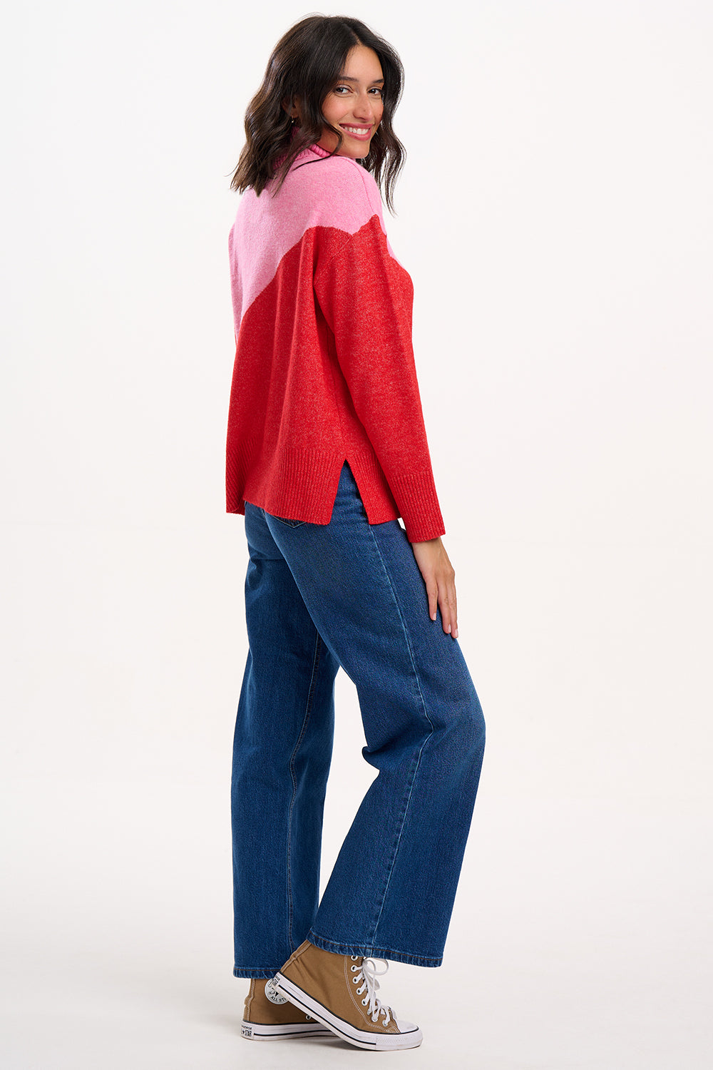 Woman wearing a red and pink top with blue jeans on a white background