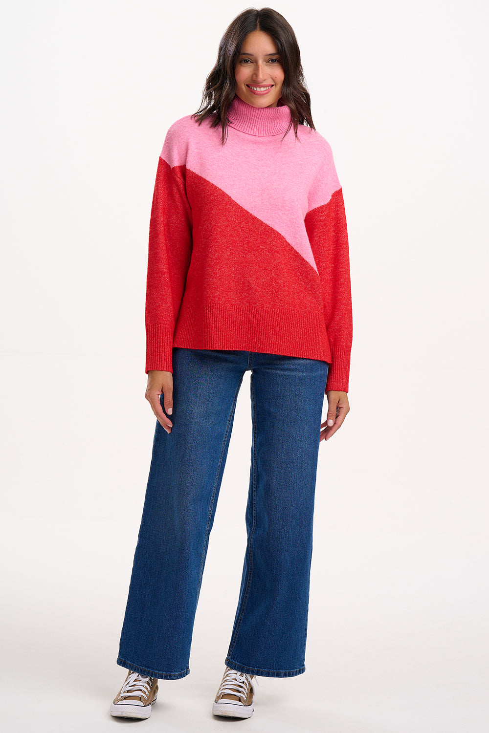 Person wearing a red and pink sweater with blue jeans on a white background