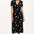 A model wearing a midi length jersey dress with a deep V-neck and short frill sleeves. The dress has a black base with a colorful hummingbird and garden design.