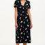 A model wearing a midi length jersey dress with a deep V-neck and short frill sleeves. The dress has a black base with a colorful hummingbird and garden design.