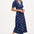 A navy midi tea dress with a multicolor pineapple print, featuring a deep V-neck and short frill sleeves, worn by a model standing against a white background.