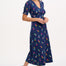 A navy midi tea dress with a multicolor pineapple print, featuring a deep V-neck and short frill sleeves, worn by a model standing against a white background.