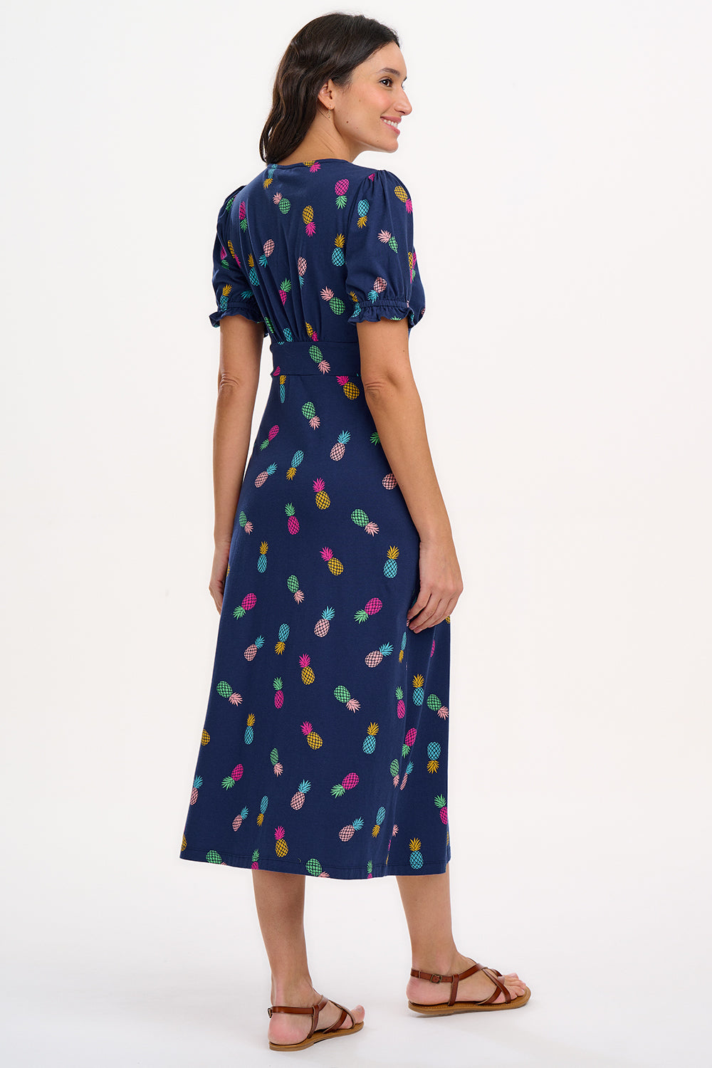 A navy midi tea dress with a multicolor pineapple print, featuring a deep V-neck and short frill sleeves, worn by a model standing against a white background.
