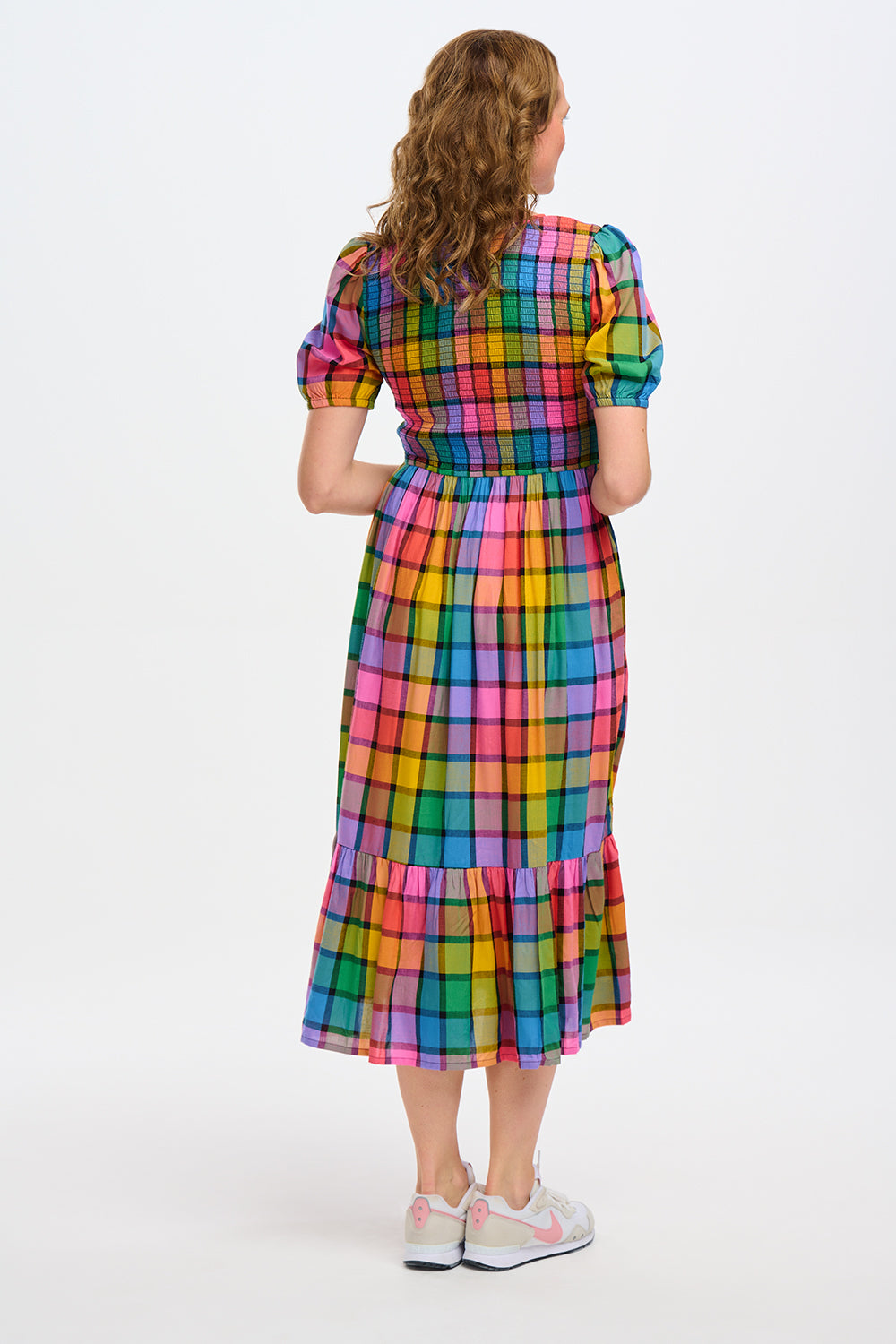 A person wearing a multicolored checkered midi dress with puff sleeves and a shirred bust, paired with sneakers, standing in front of a blue door.