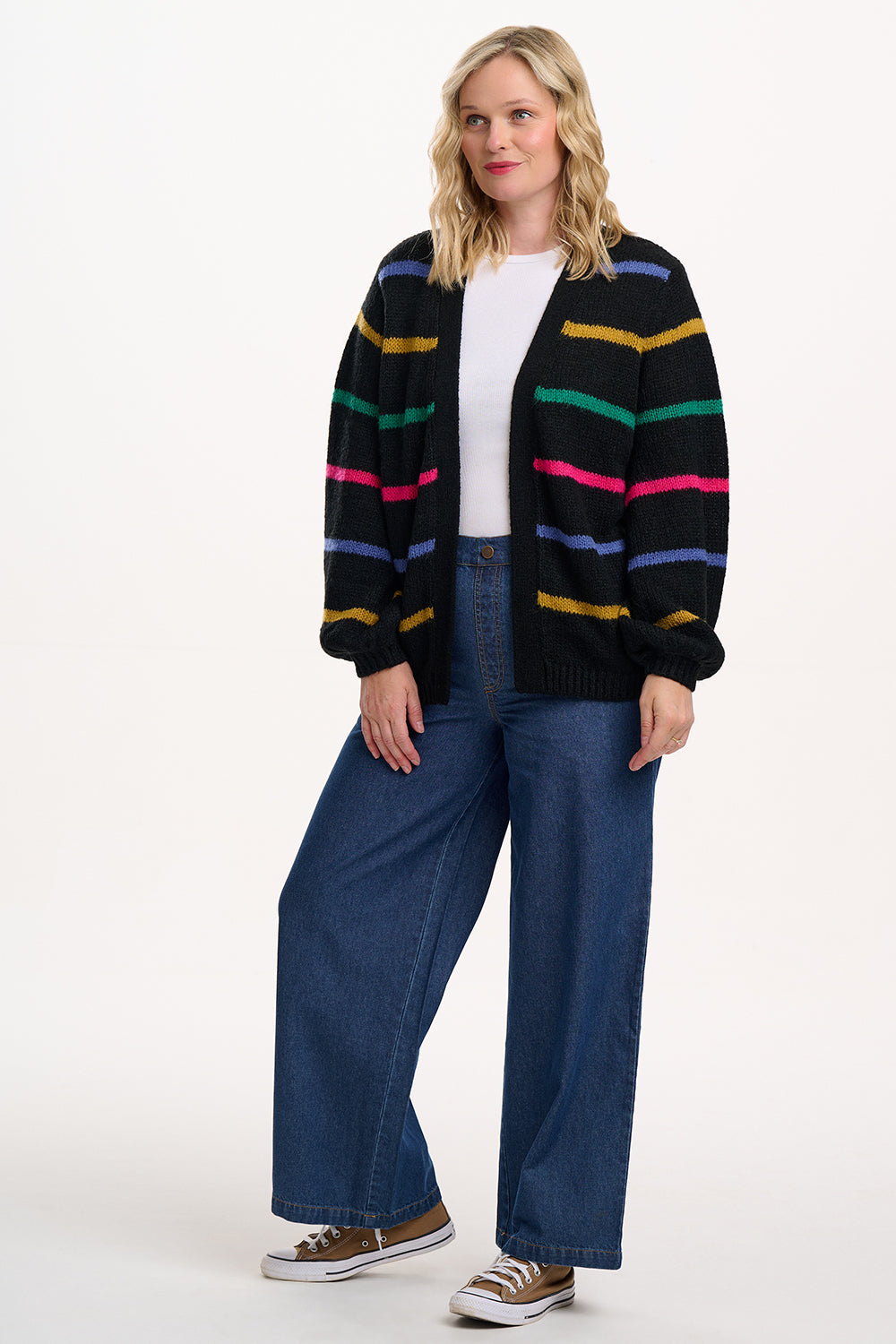 Person wearing a colorful striped cardigan and blue jeans on a white background