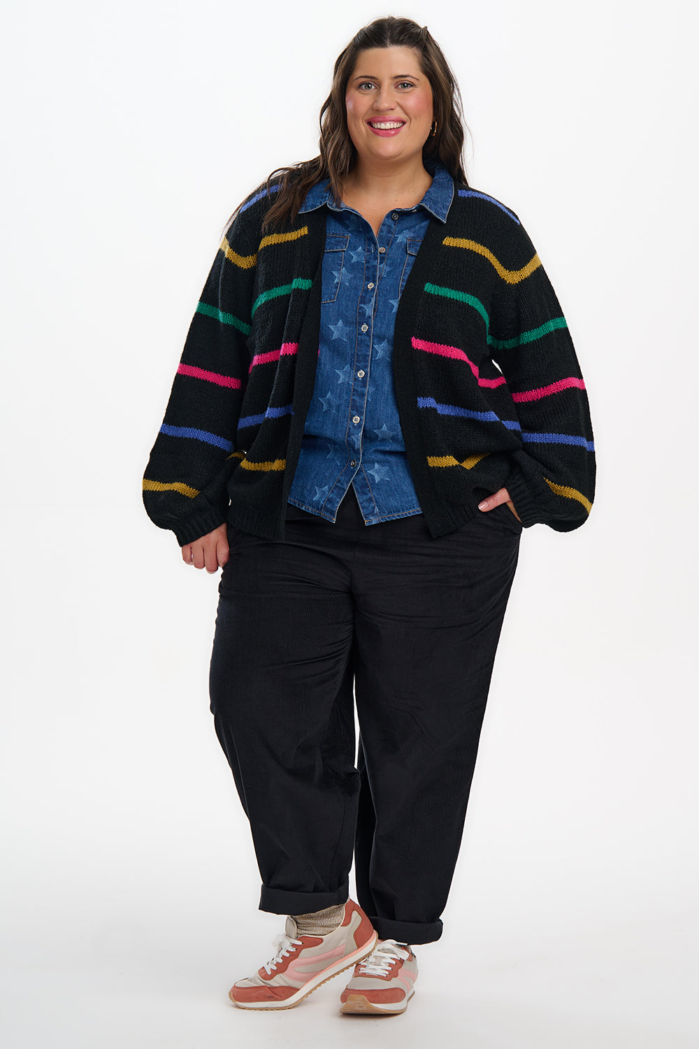 Person wearing a colorful striped cardigan over a denim jacket with black pants on a white background