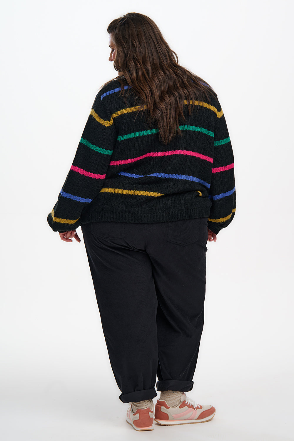 Person wearing a colorful striped sweater and black pants on a white background