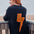 Person wearing a black sweater with an orange lightning bolt design, standing on a wooden deck by the sea.